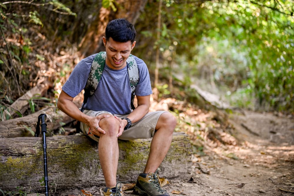 A stressed male sits on a log holding his knee, suffering from knee pain